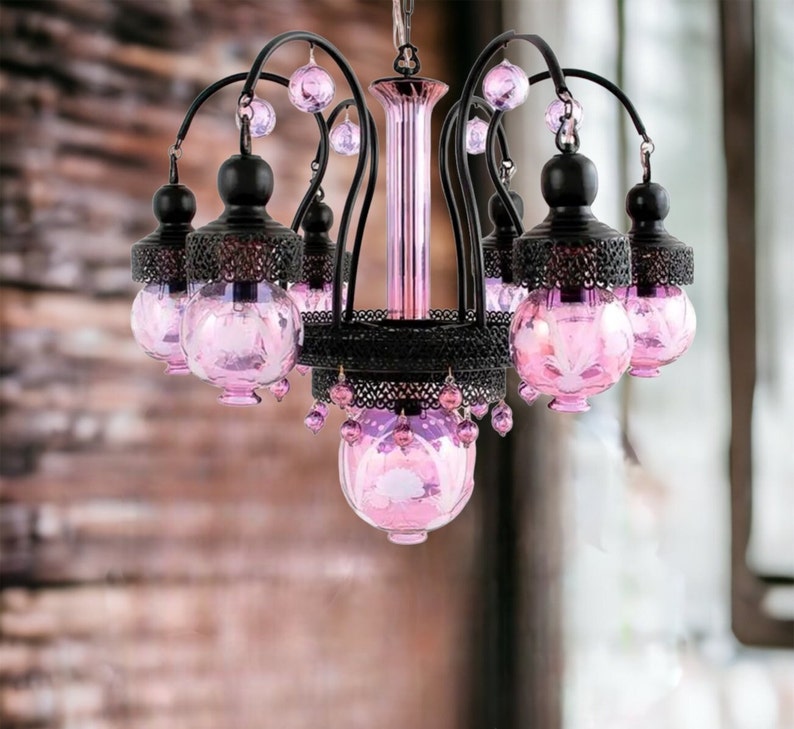 May include: A decorative chandelier with a black metal frame and six pink glass globes. The globes have a floral design and are accented with pink crystal beads. The chandelier is suspended from a chain.