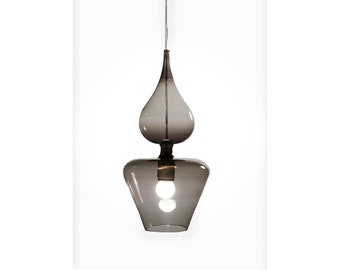 May include: A gray glass pendant light fixture with a teardrop-shaped top and a flared bottom. The light bulb is visible inside the bottom section. The fixture hangs from a thin wire against a white background.