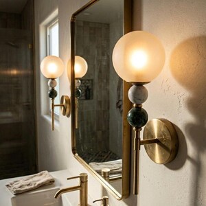 May include: A pair of wall sconces with frosted globe shades, marble accents, and brass fixtures. The sconces are mounted on a textured wall next to a mirror. The bathroom fixtures have a vintage aesthetic.