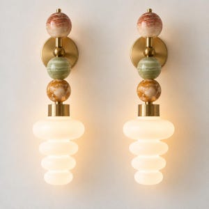 May include: A pair of wall sconces featuring a vertical arrangement of three stacked stone spheres in shades of reddish-brown, green, and amber, connected by brass hardware, ending in a tiered, frosted white glass shade.