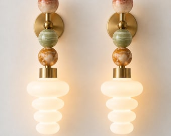 May include: A pair of wall sconces featuring a vertical arrangement of three stacked stone spheres in shades of reddish-brown, green, and amber, connected by brass hardware, ending in a tiered, frosted white glass shade.