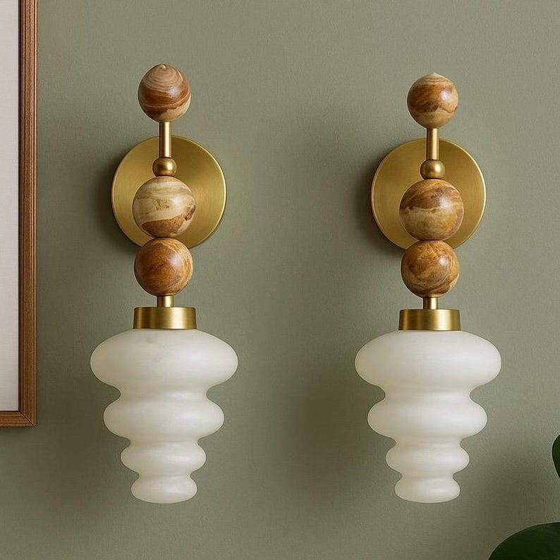 May include: A pair of wall sconces with a brass finish, featuring a stacked design of wooden spheres and a white, bulbous glass shade. The sconces are mounted on a muted green wall, creating a warm and inviting ambiance.