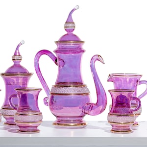 May include: A complete set of decorative glassware in shades of purple, including a large teapot, a covered container, a creamer, and several small handled glasses. The set features gold trim and a textured, frosted band around the base of each piece.
