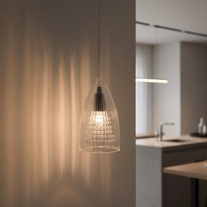 May include: A clear glass pendant light fixture with a ribbed design. The light hangs from a thin wire and illuminates a modern kitchen. The fixture has a black top and a bright light bulb.