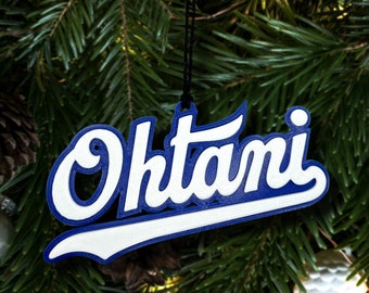 Op de afbeelding: Een blauwe en witte gepersonaliseerde kerstversiering met de naam "Ohtami" in een cursief schrift.