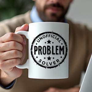 May include: White ceramic mug featuring the text "UNOFFICIAL PROBLEM SOLVER" in a black, distressed circular design. The mug has a standard handle and is held by a person.