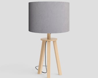 May include: A grey fabric lampshade sits atop a wooden tripod lamp base. The lamp has a black cord.