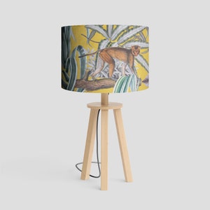 May include: A yellow lampshade with a monkey and tropical plants design. The lampshade is on a wooden tripod stand.