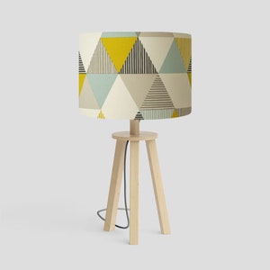 May include: A wooden table lamp with a tripod base and a drum shade featuring a geometric pattern of yellow, blue, and grey triangles.