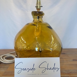 May include: Amber glass table lamp with a brass socket and a white card with the text "Seaside Shades Handmade in Cornwall".
