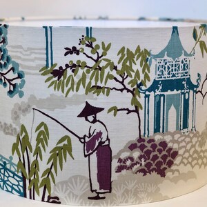 May include: A white lampshade with a blue and green Asian-inspired design. The design features a pagoda, a person fishing, and bamboo.