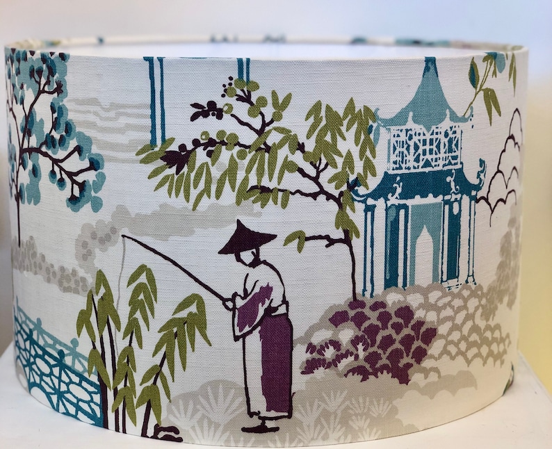 May include: A white lampshade with a blue and green Asian-inspired design. The design features a pagoda, a person fishing, and bamboo.