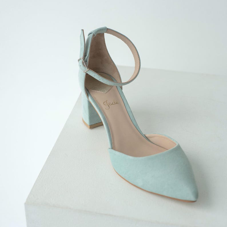 Puede incluir: Un zapato de color azul claro con punta afilada, tac&oacute;n de bloque y una correa al tobillo con hebilla plateada. La plantilla interior es de color beige y muestra el nombre de la marca Jaci en cursiva. El exterior tiene una textura mate.