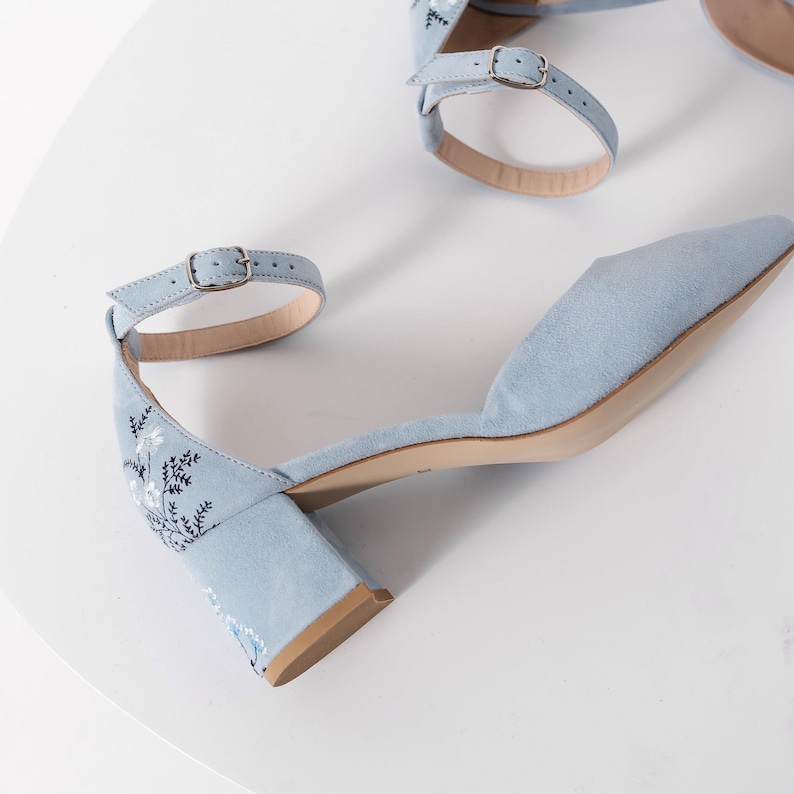 Puede incluir: Zapatos de tac&oacute;n de ante azul claro con un dise&ntilde;o de bordado floral y una correa de tobillo con cierre de hebilla.
