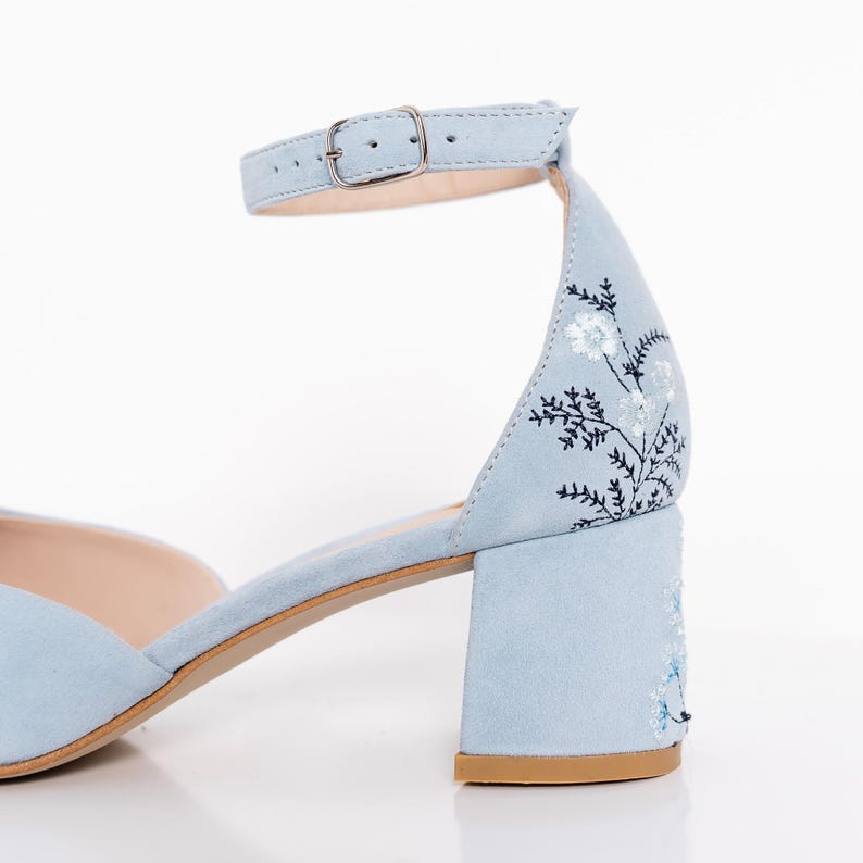 Puede incluir: Sandalias de tac&oacute;n de ante azul claro con correa de tobillo y bordado floral. El tac&oacute;n es un tac&oacute;n de bloque.