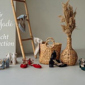 K&ouml;nnte beinhalten: Eine Kollektion von Schuhen in Hellblau, Rot, Schwarz und Dunkelgr&uuml;n mit Kn&ouml;chelriemen und Blockabs&auml;tzen, dazu ein geflochtener Korb und eine hohe Vase mit getrocknetem Gras. Der Text Utz & Jad&eacute; Tracht Collection ist zu sehen.