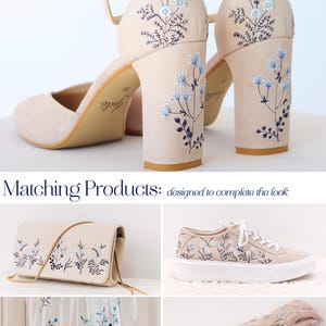 May include: Beige block-heel shoes with ankle straps and blue floral embroidery on the heels. Matching products include a beige clutch with a gold chain, beige trainers with white soles, a white veil, and sheer gloves, all featuring blue floral embroidery.