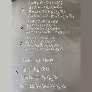 May include: A white fabric with four rows of the alphabet, A through Z, in cursive script. Each row is numbered 1 through 4.