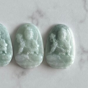 以下が含まれることがあります： 花を持った座った人物の彫刻が施された、翡翠製のペンダントが3つ。ペンダントは薄い緑色で、滑らかで磨かれた仕上げになっています。