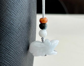May include: A white jade pendant carved in the shape of a rat, hanging from a white cord with three beads: orange, black, and white.