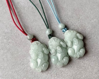 May include: Three jade pendants in the shape of a crouching animal, each on a different colored cord. The cords are red, green, and blue.