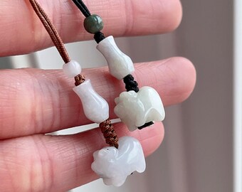 May include: Two jade pendants on thin cords. One pendant features a white carved animal figure and a vase-shaped bead on a brown cord. The other pendant has a white carved animal figure, a vase-shaped bead, and a small green bead on a black cord.