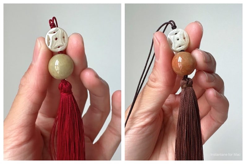 Puede incluir: Un borla decorativa con una cuenta blanca tallada, una cuenta redonda verde y una borla roja. La borla es sostenida por una mano sobre un fondo blanco. La segunda imagen muestra una borla similar con una borla marr&oacute;n.