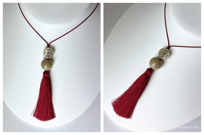 Puede incluir: Un collar con borlas burdeos con un cord&oacute;n rojo. El collar presenta dos cuentas redondas, una con un dise&ntilde;o estampado, y una cuenta m&aacute;s grande de color s&oacute;lido. La borla es larga y completa, a&ntilde;adiendo un toque dram&aacute;tico a la joya.