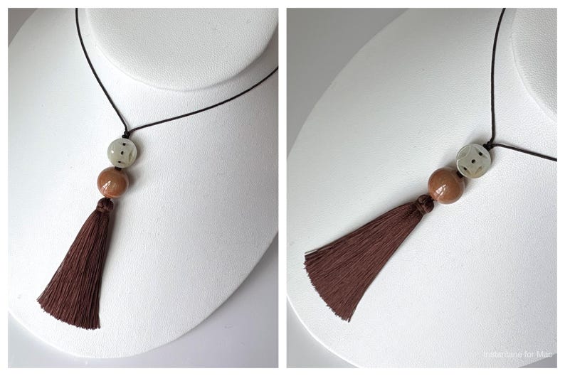 Puede incluir: Un collar con un cord&oacute;n negro, con una cuenta clara estampada, una cuenta marr&oacute;n y una borla marr&oacute;n. El collar se exhibe en un busto de maniqu&iacute; blanco, mostrando su dise&ntilde;o y longitud.