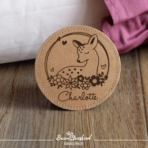 Könnte beinhalten: Ein runder, hölzerner Untersetzer mit einem Laser-gravierten Design eines Rehs mit Blumen und dem Namen "Charlotte".