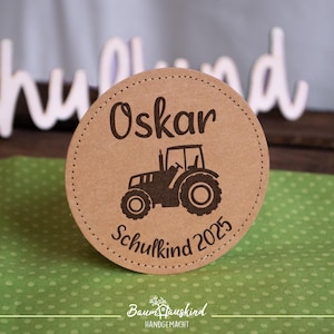 Könnte beinhalten: Brauner Papierkreis mit einer Traktorsilhouette und dem Text "Oskar Schulkind 2023".