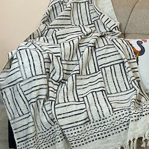 Könnte beinhalten: Eine weiße und schwarze gestreifte Wolldecke mit geometrischem Muster und Fransenbesatz. Die Decke liegt auf einem Sofa.