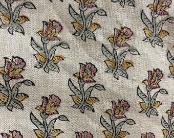 Op de afbeelding: Een beige stof met een herhalend patroon van roze en gele bloemen. De bloemen hebben een eenvoudig ontwerp met vijf bloemblaadjes en zijn zwart omlijnd.