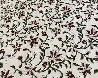 Puede incluir: Tela blanquecina con un estampado floral repetido. El diseño presenta flores marrones y hojas verdes sobre tallos sinuosos. Las flores tienen múltiples pétalos y las hojas son de color verde oscuro. El patrón general es denso y cubre toda la tela.