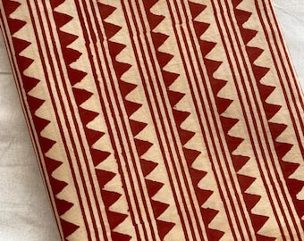 May include: Red and cream fabric with a geometric pattern of triangles and stripes. The fabric is folded in half and lying on a white surface.