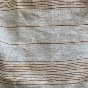 May include: A close-up of a white fabric with thin brown stripes. The fabric has a textured, woven appearance.