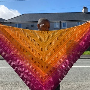 May include: A crocheted shawl with a gradient of pink, orange, and yellow. The shawl is triangular in shape and has a lacy pattern.