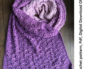 May include: A purple and white ombre crochet scarf with a delicate stitch pattern. The scarf is folded in half and draped over a wooden surface.