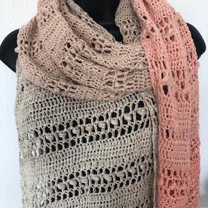 May include: A crocheted shawl in a light brown and peach color gradient. The shawl is made with a delicate openwork pattern and has a fringed edge.