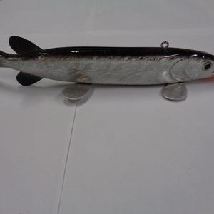 May include: A silver and black fish-shaped lure with a red mouth. The lure has a black top, silver sides, and two small silver fins. A small metal ring is attached to the top of the lure. The lure is designed for fishing.