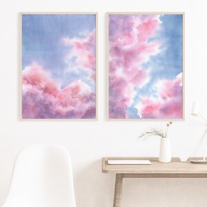 Puede incluir: Dos pinturas de acuarela enmarcadas de nubes rosas y azules. Las pinturas est&aacute;n colgadas una al lado de la otra en una pared blanca.