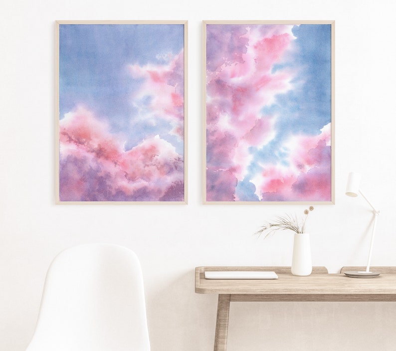 Puede incluir: Dos pinturas de acuarela enmarcadas de nubes rosas y azules. Las pinturas est&aacute;n colgadas una al lado de la otra en una pared blanca.