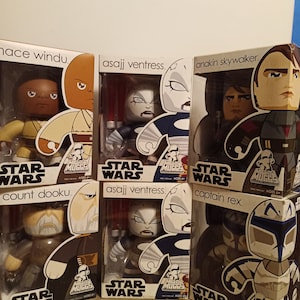 Może przedstawiać: Sześć kolekcjonerskich figurek Star Wars Mighty Muggs w opakowaniu. Figurki obejmują Mace Windu, Asajj Ventress, Anakina Skywalkera, Hrabiego Dooku, Asajj Ventress i Kapitana Rexa. Opakowanie jest białe z czerwonymi i niebieskimi akcentami i zawiera logo Star Wars.
