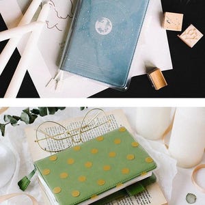 Puede incluir: Dos cuadernos con cubiertas de pl&aacute;stico transparente. El cuaderno de arriba tiene una cubierta azul con un dise&ntilde;o blanco de un globo terr&aacute;queo rodeado de estrellas. El cuaderno de abajo tiene una cubierta verde con un patr&oacute;n de lunares dorados.