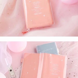 Puede incluir: Dos cuadernos de color rosa con cubierta de pl&aacute;stico transparente y un dise&ntilde;o de estrellas y luna blancas. El texto en el cuaderno dice "One moon turns into a clock, the brightest stars look at me with your eyes".