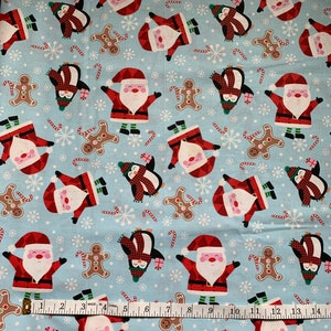May include: Light blue Christmas-themed fabric with repeating patterns of Santa Claus, penguins in plaid scarves, gingerbread men, candy canes, and snowflakes. A measuring tape is laid across the bottom of the fabric.