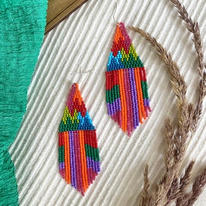 May include: A pair of colourful beaded fringe earrings with a geometric pattern. The earrings are made with red, orange, yellow, green, blue, purple and pink beads.