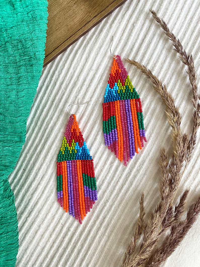 May include: A pair of colourful beaded fringe earrings with a geometric pattern. The earrings are made with red, orange, yellow, green, blue, purple and pink beads.