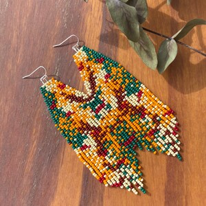 May include: A pair of long, beaded earrings with a geometric pattern in shades of green, orange, red, brown, and white.