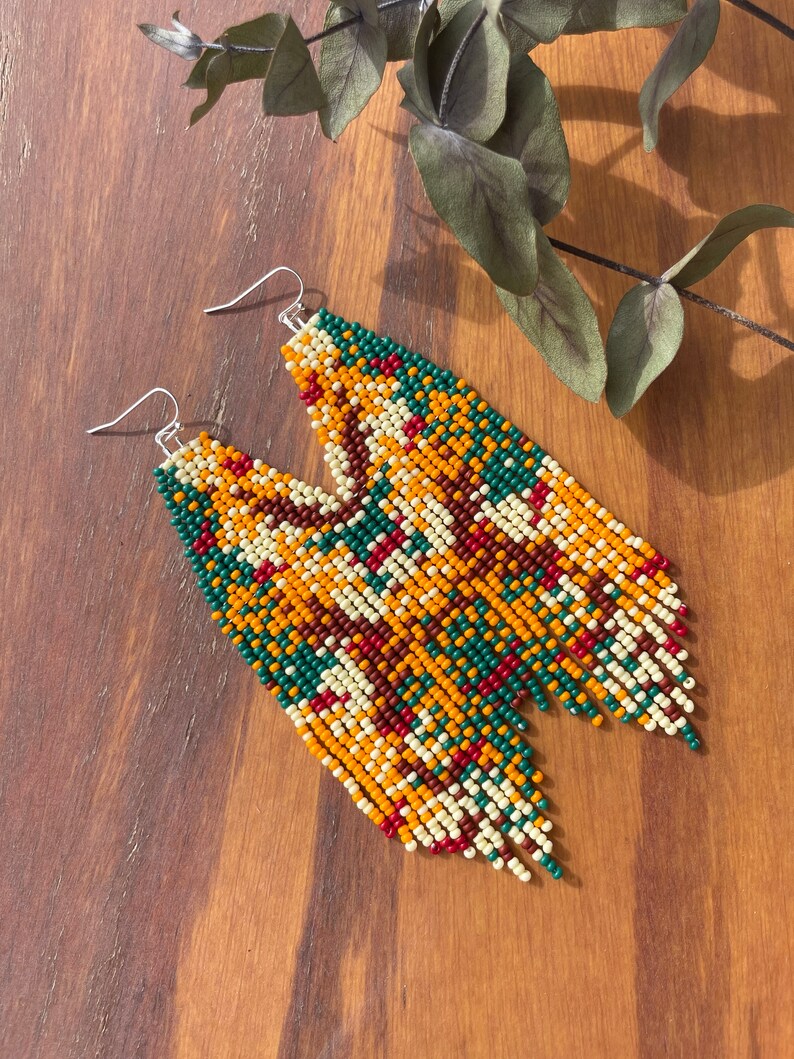 May include: A pair of long, beaded earrings with a geometric pattern in shades of green, orange, red, brown, and white.